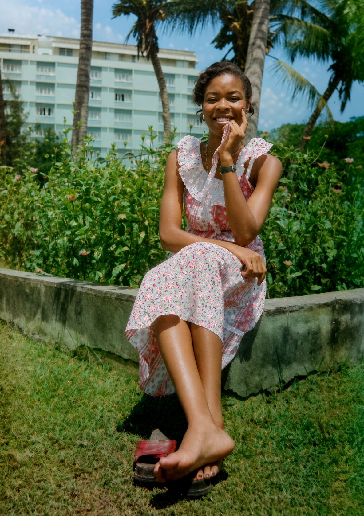 Gloria Nzenwa seated on a garden wall in a pink floral dress